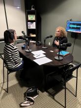 Carrie sits at podcast interview desk with Pam